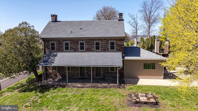 back of property with a chimney, a patio area, a yard, and stone siding