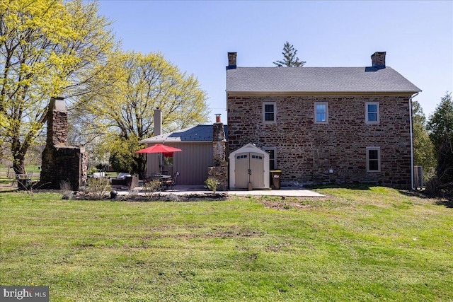 rear view of property with a chimney, a yard, a patio, and a shed
