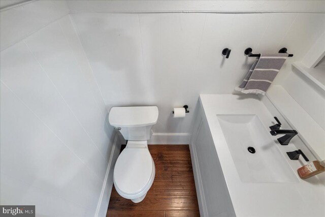half bathroom with toilet, a sink, wood finished floors, and baseboards