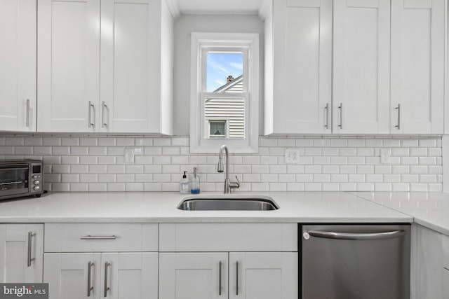 kitchen with stainless steel dishwasher, a sink, white cabinets, and backsplash
