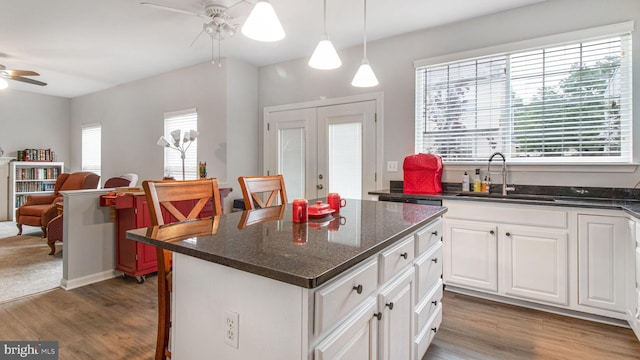 kitchen featuring ceiling fan, a sink, wood finished floors, white cabinets, and a kitchen island