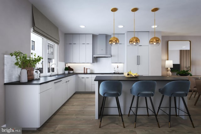 kitchen with dark countertops, a kitchen breakfast bar, a sink, and wall chimney range hood