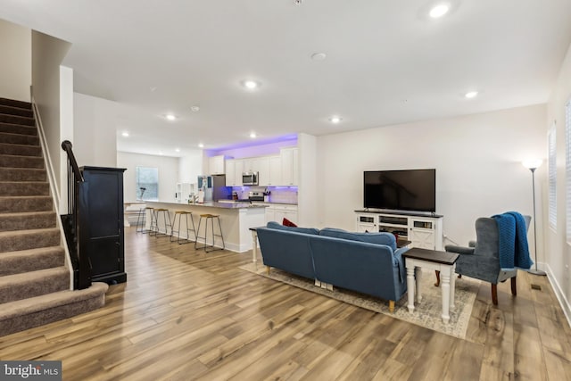 living room featuring baseboards, stairs, light wood finished floors, and recessed lighting