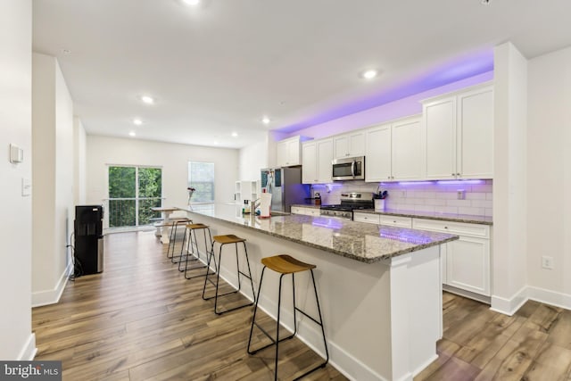 kitchen featuring tasteful backsplash, a spacious island, a breakfast bar, stainless steel appliances, and white cabinetry