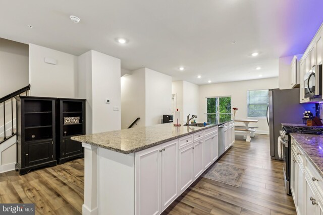 kitchen featuring white cabinets, a sink, a center island with sink, wood finished floors, and appliances with stainless steel finishes