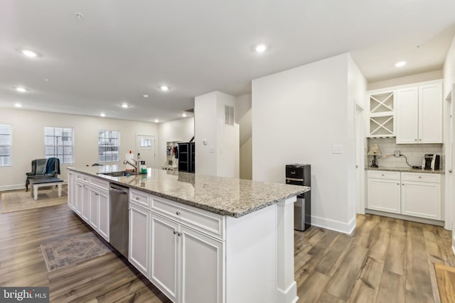 kitchen with white cabinets, light wood finished floors, dishwasher, a center island with sink, and decorative backsplash