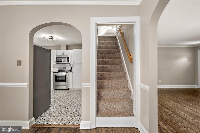 stairs with arched walkways, baseboards, crown molding, and wood finished floors