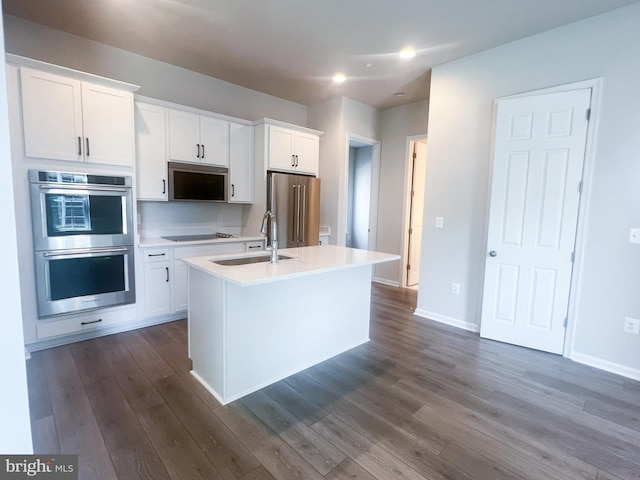 kitchen with a sink, white cabinets, dark wood-style floors, stainless steel appliances, and an island with sink