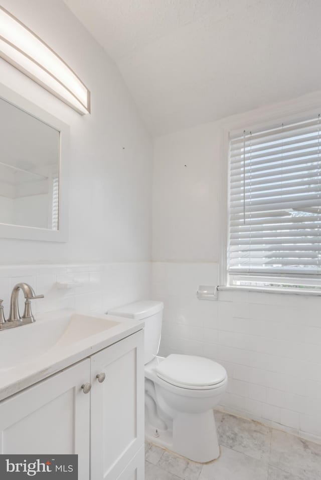 647 Emerson St NE, Washington, DC 20017 - bathroom with tile walls, vaulted ceiling, vanity, and toilet