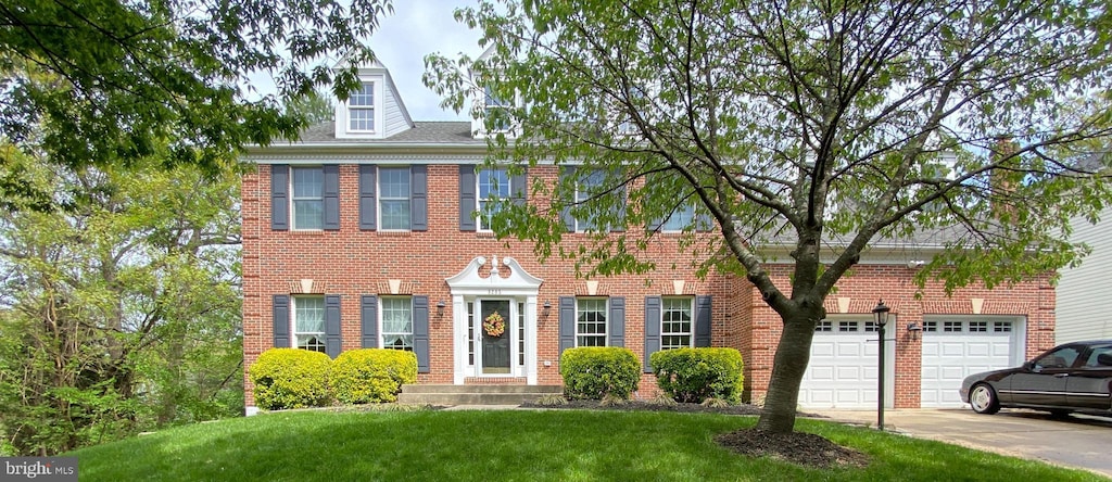 colonial inspired home with brick siding, a front lawn, and driveway