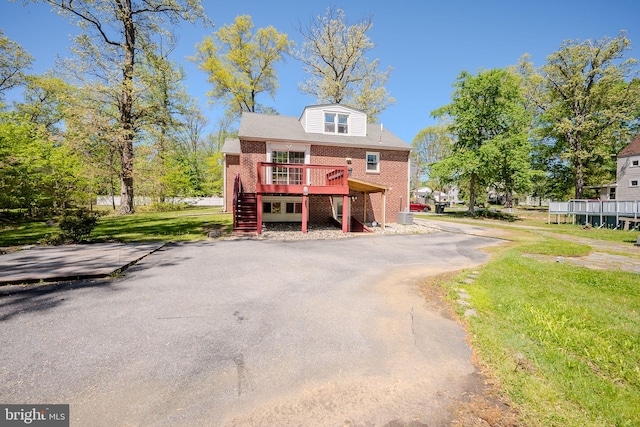 view of front facade with brick siding, stairs, a front yard, and a deck