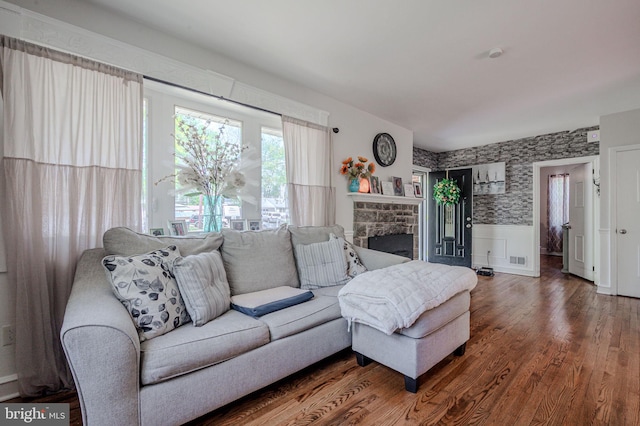 living area featuring wainscoting, a stone fireplace, wallpapered walls, wood finished floors, and visible vents