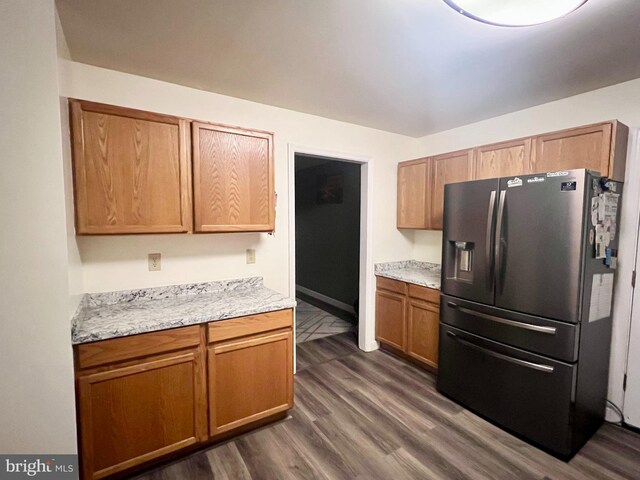 kitchen with dark wood-type flooring, brown cabinetry, baseboards, and refrigerator with ice dispenser