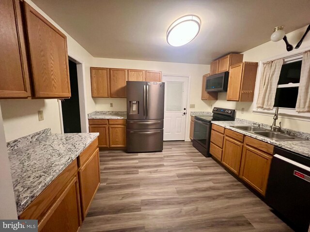 kitchen with light wood-style flooring, a sink, brown cabinets, light stone counters, and black appliances