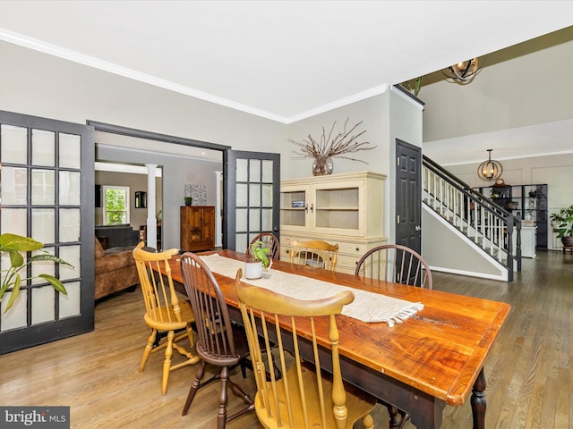 dining space featuring stairs, wood finished floors, ornamental molding, french doors, and ornate columns
