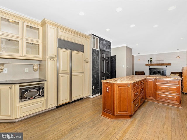 kitchen featuring cream cabinets, paneled built in refrigerator, a fireplace, ornamental molding, and light wood-style flooring