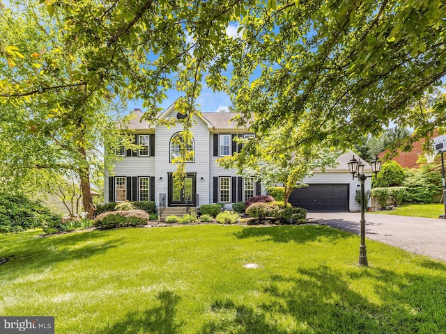 colonial inspired home featuring asphalt driveway, a front yard, and an attached garage