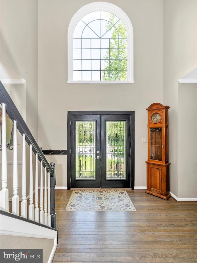 foyer entrance featuring a towering ceiling, plenty of natural light, stairs, french doors, and wood finished floors