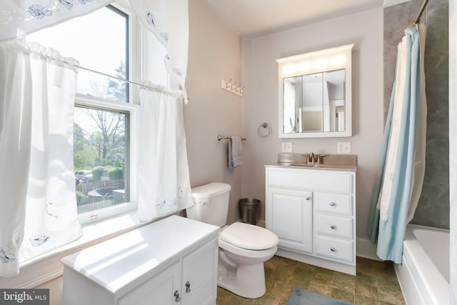 bathroom featuring stone finish flooring, vanity, toilet, and a healthy amount of sunlight