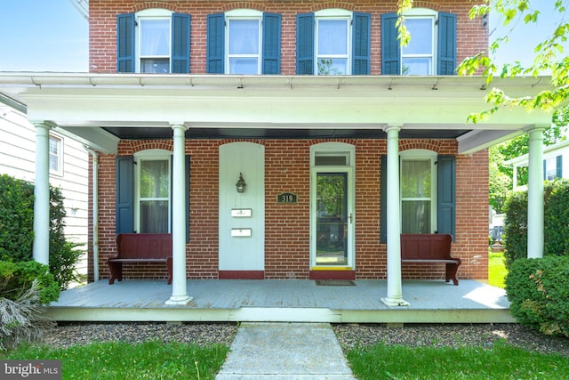 view of exterior entry with a porch and brick siding