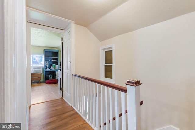 corridor with wood finished floors, vaulted ceiling, and an upstairs landing