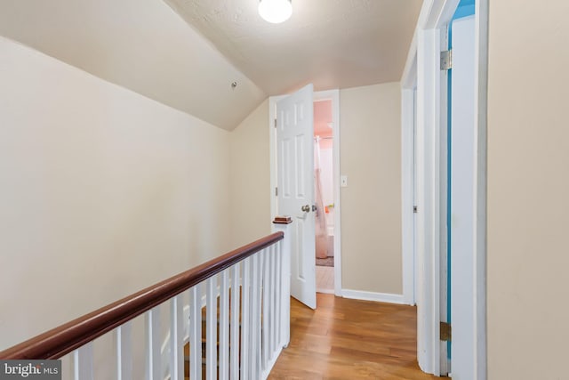 hallway with light wood finished floors, vaulted ceiling, and baseboards