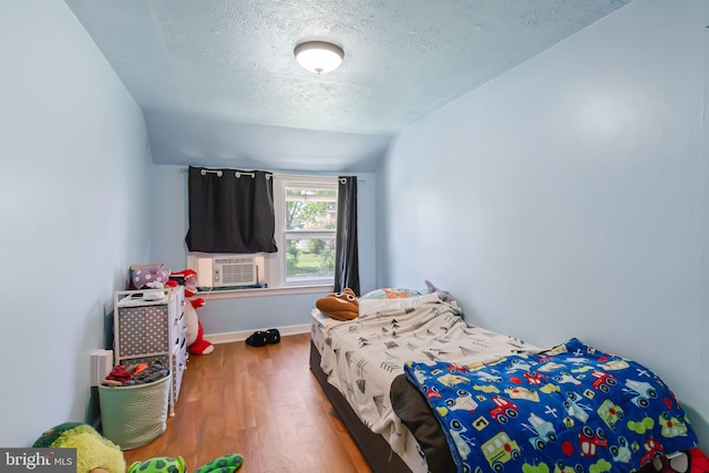 bedroom with lofted ceiling, a textured ceiling, baseboards, cooling unit, and wood finished floors