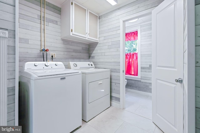 laundry area with cabinet space, washing machine and dryer, light tile patterned floors, and wooden walls