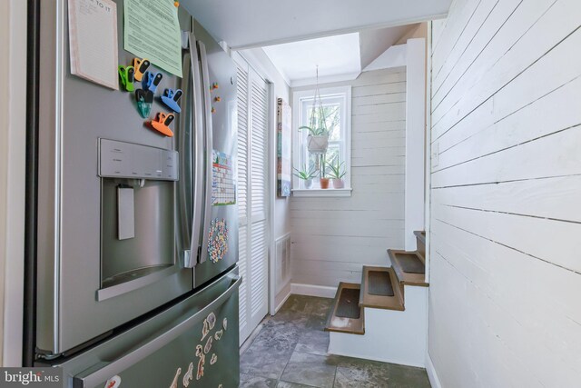 kitchen featuring stone finish floor, stainless steel fridge with ice dispenser, visible vents, baseboards, and wooden walls