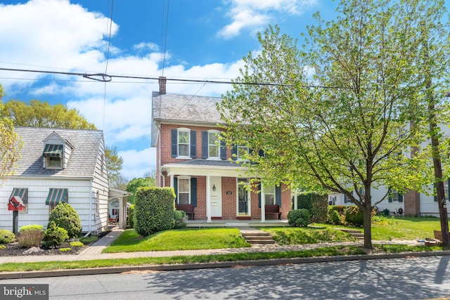 view of front of property with covered porch, a chimney, a front lawn, and brick siding