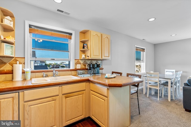 kitchen featuring light brown cabinetry, open shelves, a sink, a kitchen breakfast bar, and visible vents