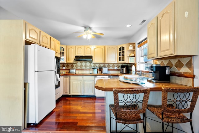 kitchen featuring visible vents, a peninsula, a breakfast bar, under cabinet range hood, and white appliances