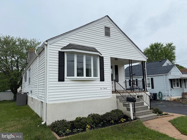 bungalow-style home featuring a chimney, central AC, and a front yard
