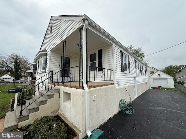 view of front of property with a detached garage, an outdoor structure, a porch, and aphalt driveway
