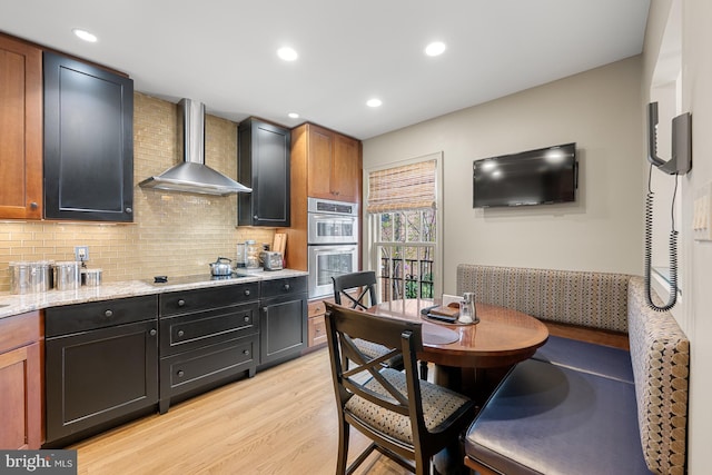 4360 Westover Pl NW, Washington, DC 20016 - kitchen featuring light wood finished floors, double oven, wall chimney range hood, decorative backsplash, and light stone counters