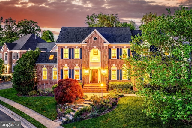 colonial house featuring a lawn, brick siding, and roof with shingles