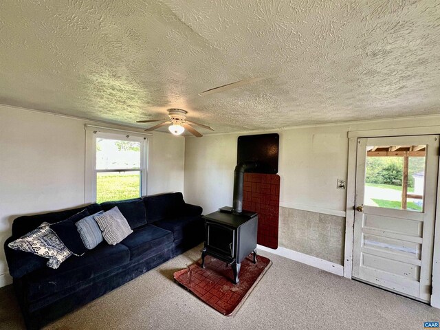 living area with carpet floors, a ceiling fan, a textured ceiling, and a wood stove