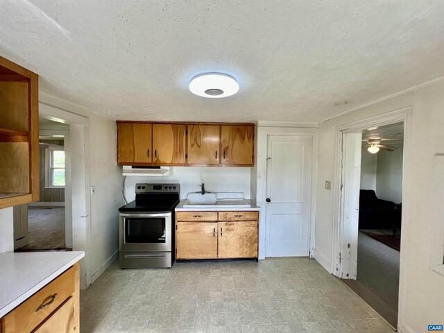 kitchen with stainless steel range with electric cooktop, light countertops, brown cabinetry, light floors, and under cabinet range hood