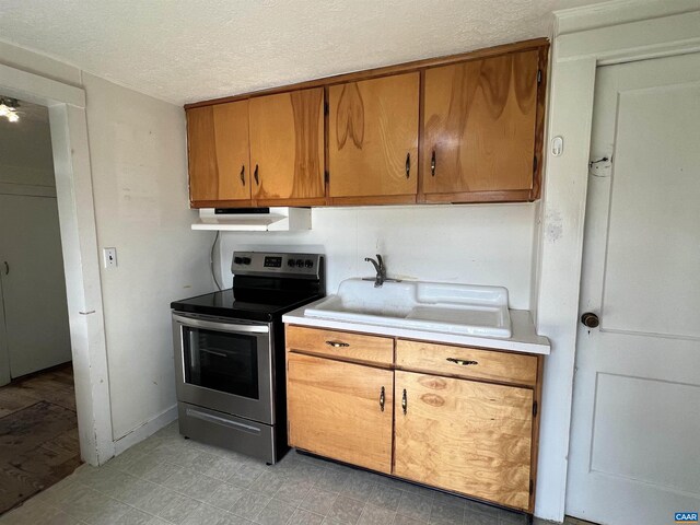 kitchen featuring a textured ceiling, stainless steel electric range oven, light countertops, light floors, and under cabinet range hood