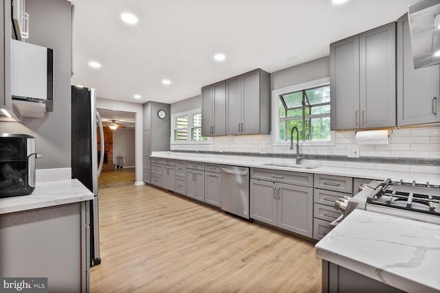kitchen with stainless steel appliances, a sink, gray cabinetry, light wood-style flooring, and tasteful backsplash
