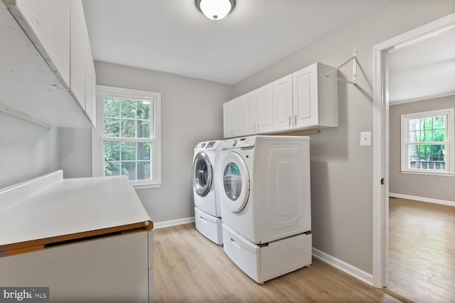 clothes washing area with cabinet space, separate washer and dryer, light wood-type flooring, and baseboards
