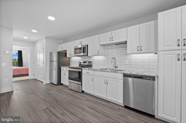 kitchen featuring white cabinets, light stone counters, stainless steel appliances, backsplash, and a sink