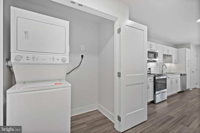 laundry area featuring dark wood-style floors, laundry area, a sink, stacked washing maching and dryer, and baseboards
