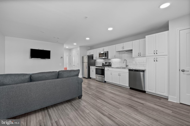 kitchen featuring a sink, decorative backsplash, open floor plan, white cabinetry, and appliances with stainless steel finishes