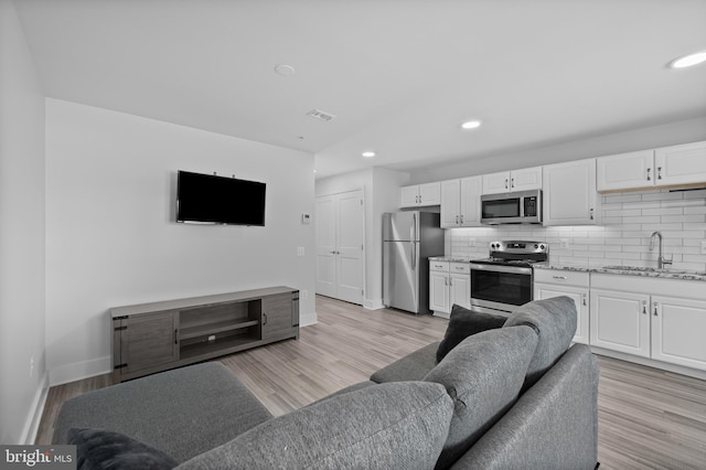 living area with recessed lighting, visible vents, light wood finished floors, and baseboards