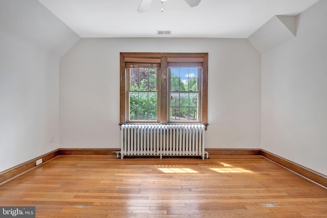 additional living space featuring radiator, vaulted ceiling, visible vents, a ceiling fan, and hardwood / wood-style flooring