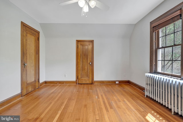 spare room featuring light wood-type flooring, vaulted ceiling, baseboards, and radiator