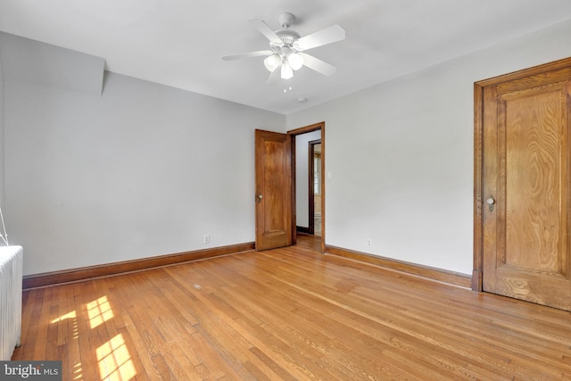 unfurnished bedroom featuring light wood finished floors, baseboards, ceiling fan, and radiator