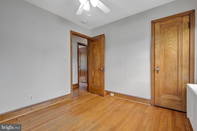 unfurnished bedroom with ceiling fan, radiator heating unit, baseboards, and light wood-type flooring