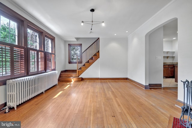 unfurnished living room with arched walkways, radiator heating unit, light wood finished floors, and baseboards